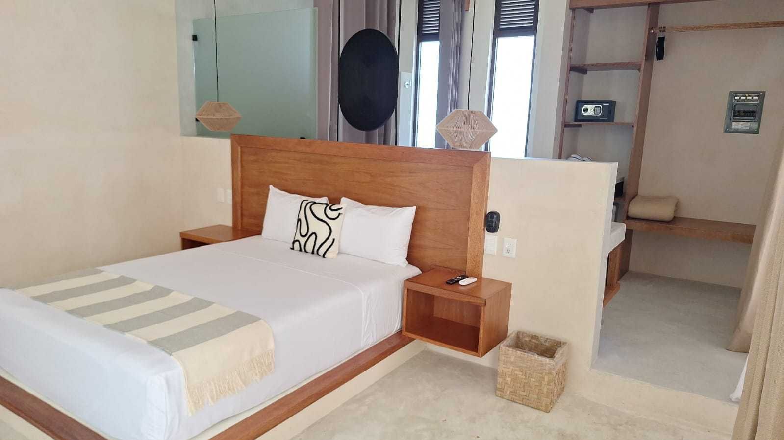 Dormitorio moderno con cama de madera, sábanas blancas, mesita de noche y baño abierto.