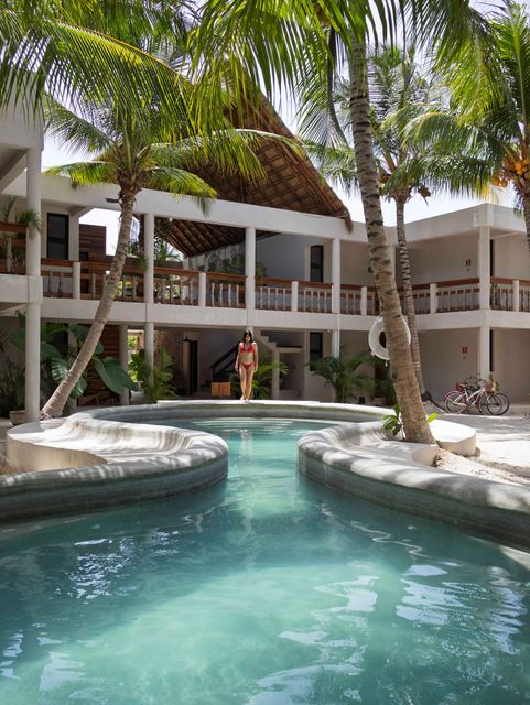 Piscina tropical en un complejo turístico rodeada de exuberantes palmeras y tumbonas bajo un cielo azul.