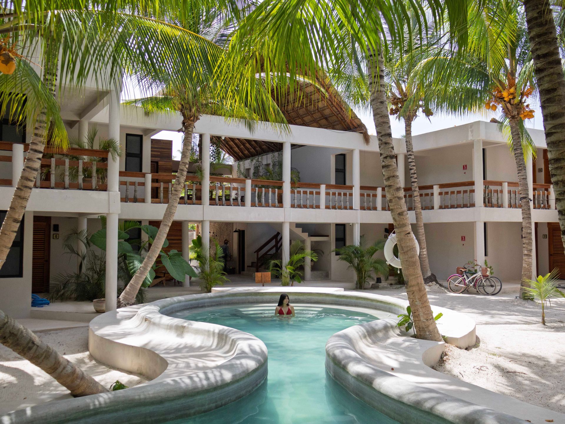 Patio bordeado de palmeras con una pequeña piscina y edificios blancos de dos plantas a su alrededor.