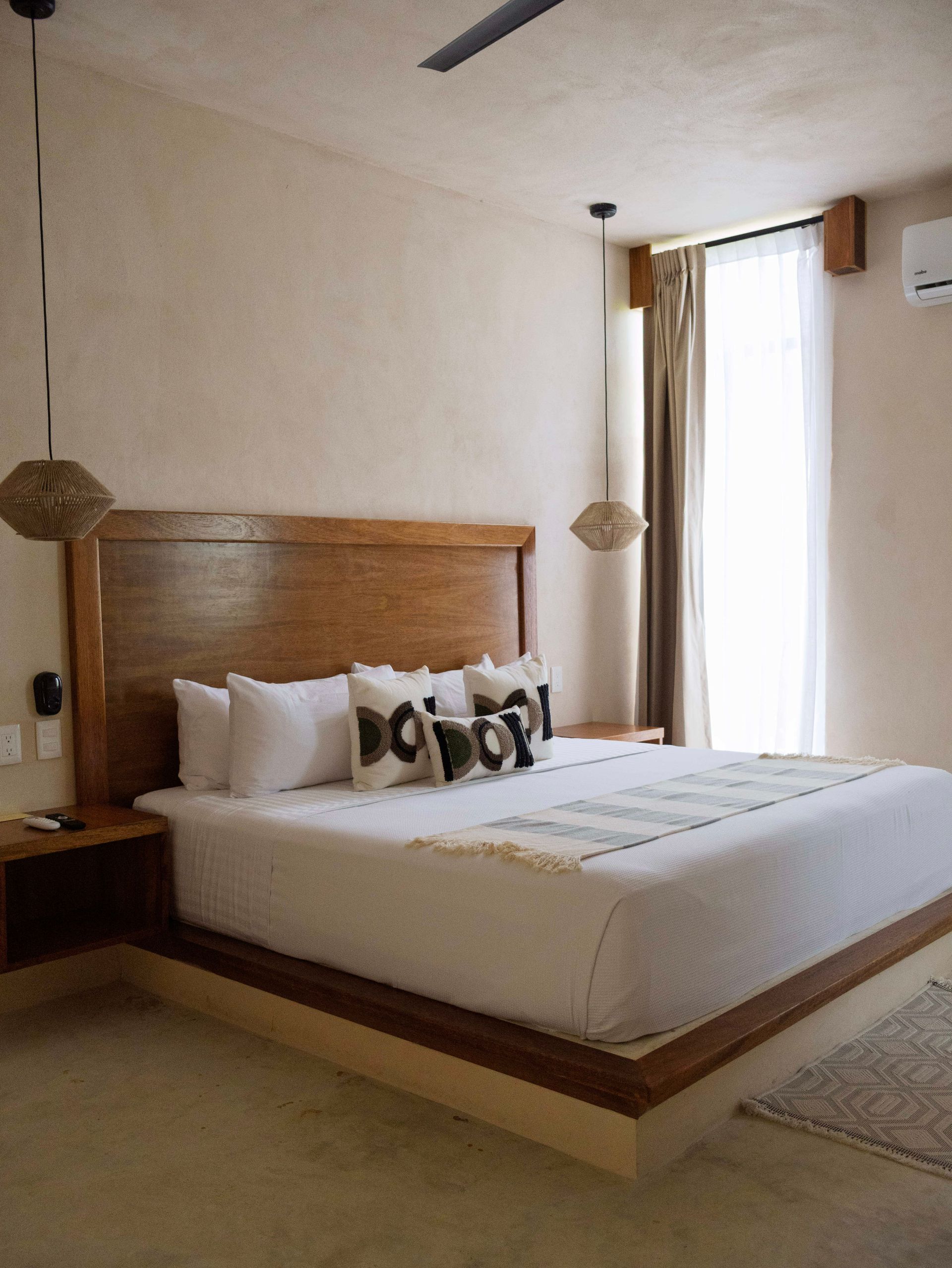 Dormitorio moderno con cama de madera, ropa de cama blanca y una ventana luminosa con cortinas.