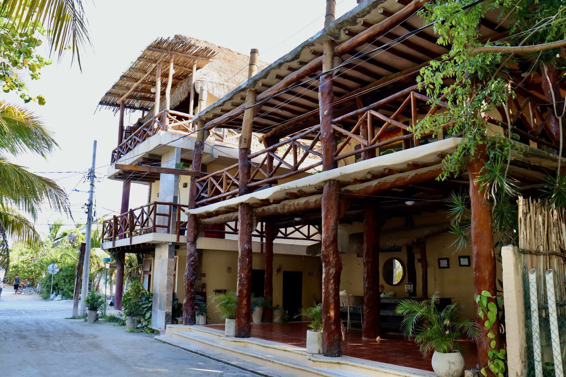 Cabaña de madera al aire libre con balcones y un paseo sombreado junto a una carretera arbolada.