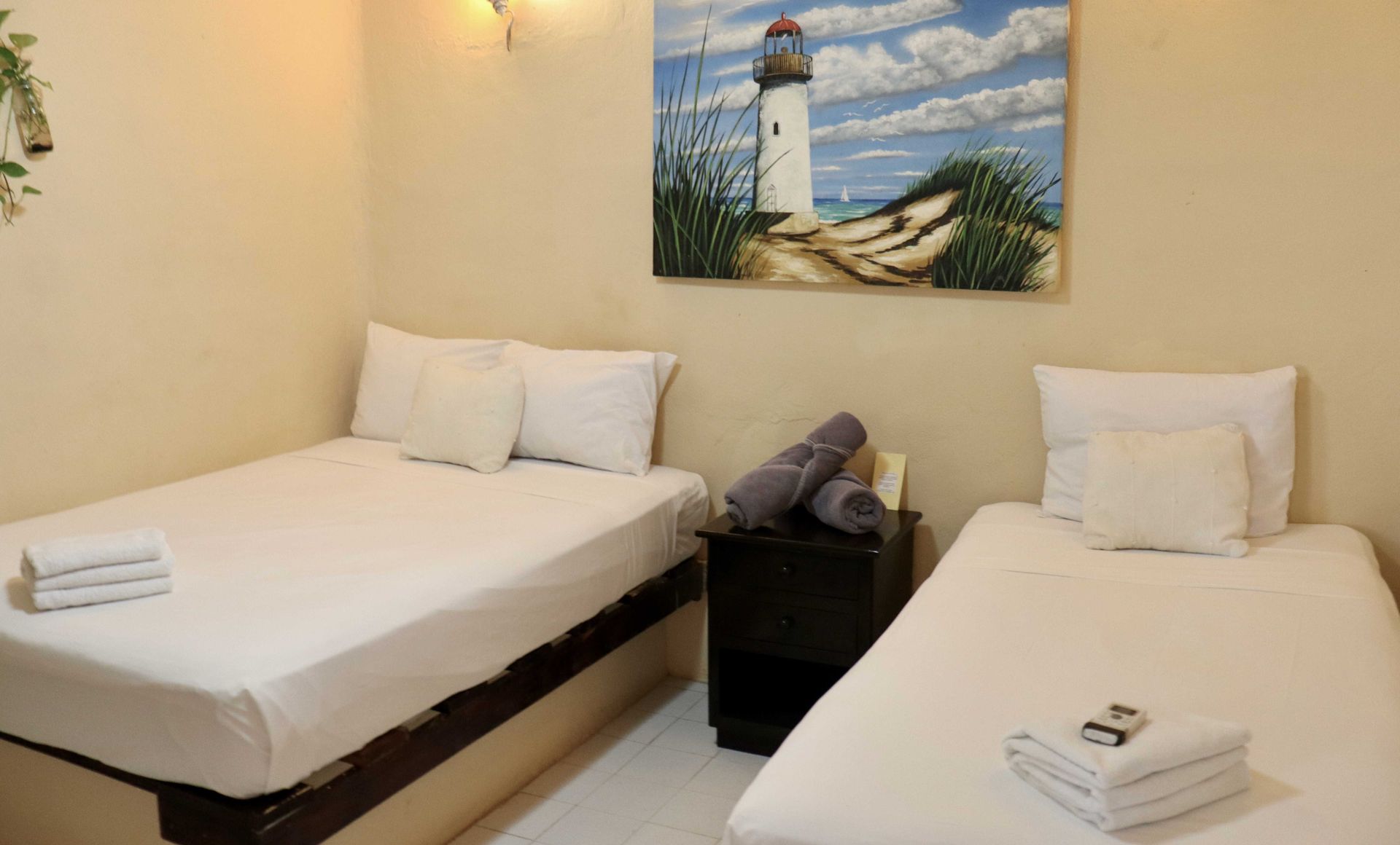 Habitación de hotel pequeña con dos camas individuales bien hechas, mesita de noche y cuadro de un faro en la pared.