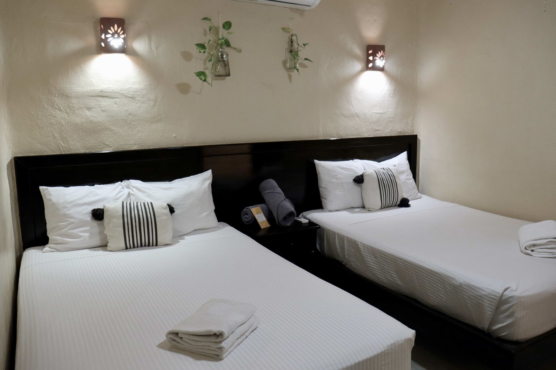 Dos camas individuales bien hechas con sábanas blancas en un dormitorio con iluminación tenue.