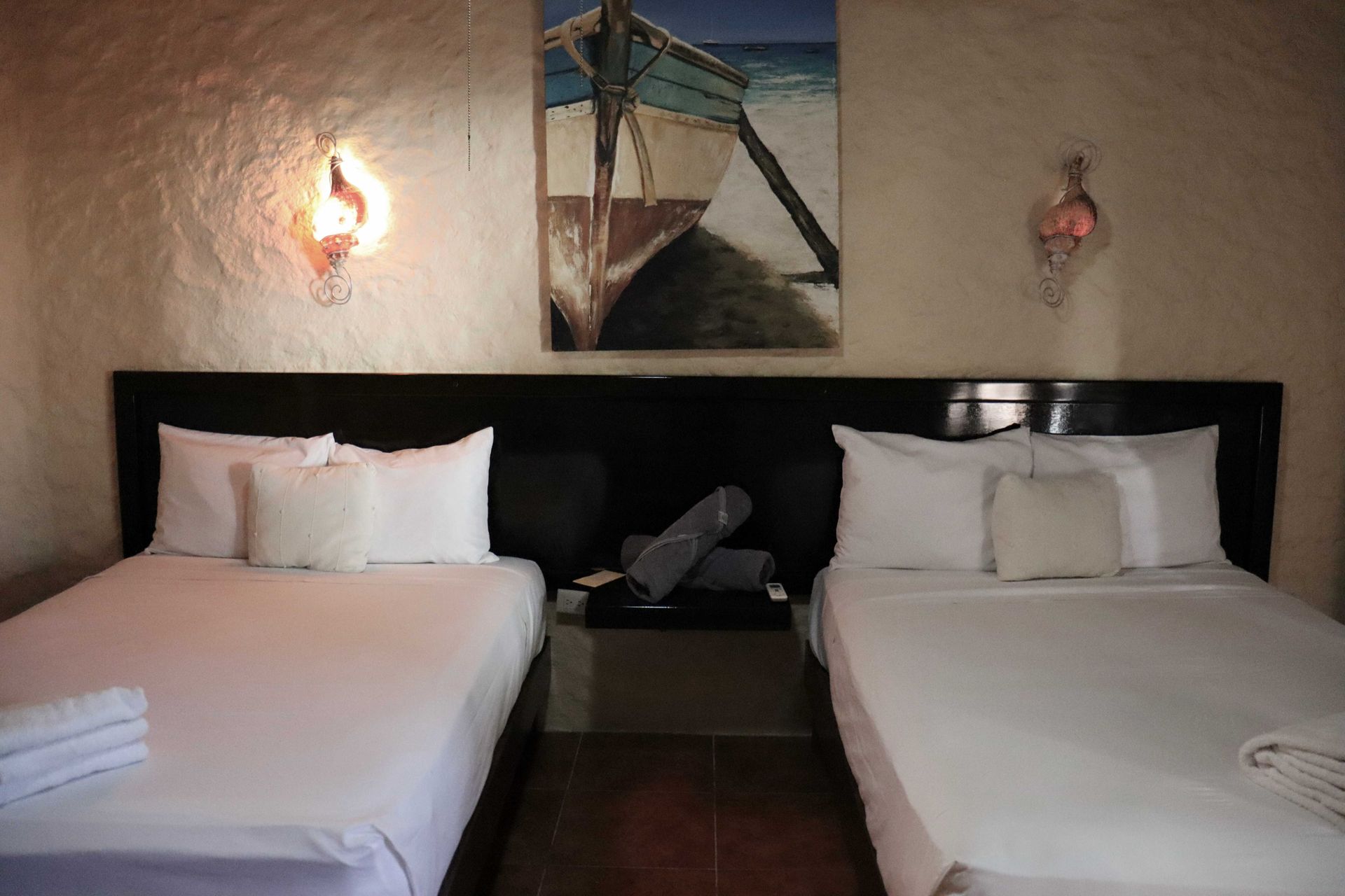 Habitación de hotel con dos camas individuales, cuadros en la pared y una lámpara de luz cálida entre ellas.