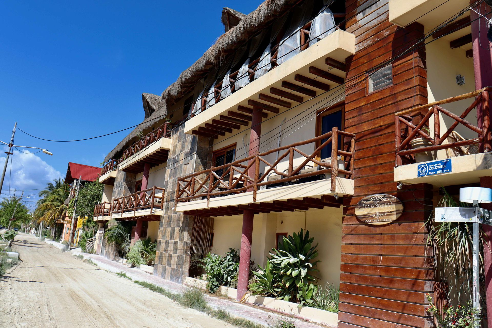 Calle soleada con balcones rústicos de madera en una hilera de edificios de ladrillo bajo un cielo azul.
