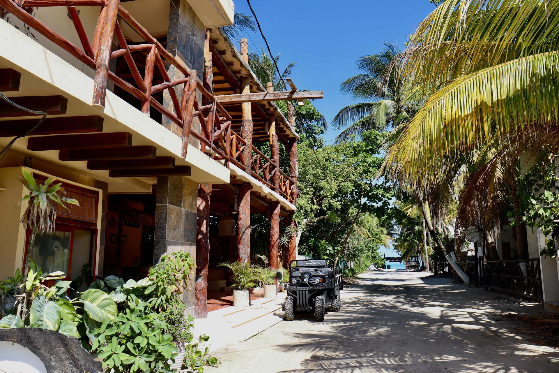 Calle soleada junto a un edificio tropical con palmeras y un jeepney estacionado.