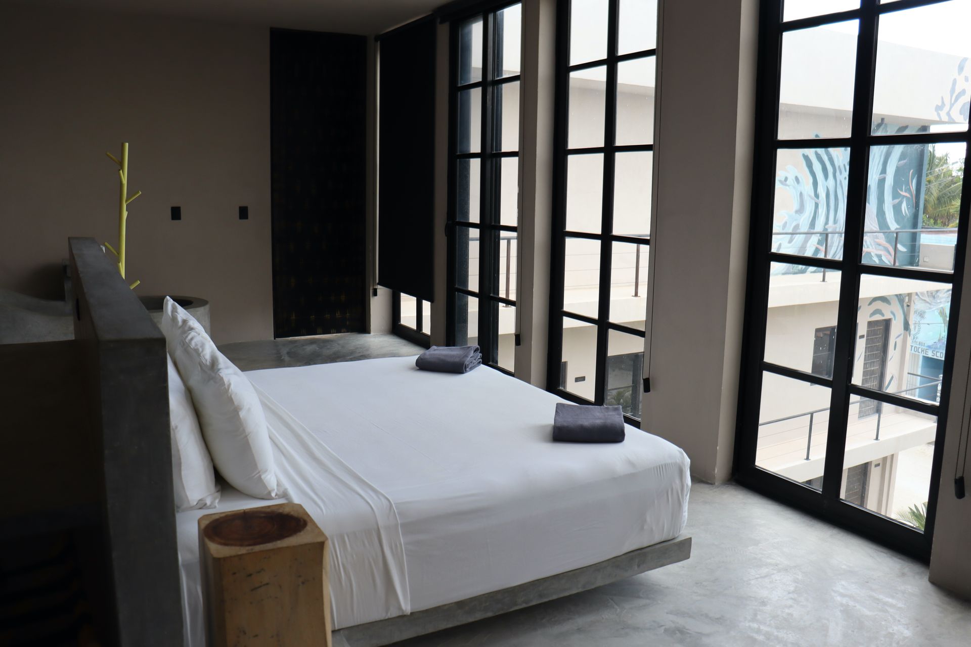 Habitación moderna con una cama grande, sábanas blancas y ventanales que van del suelo al techo con vistas a un balcón.