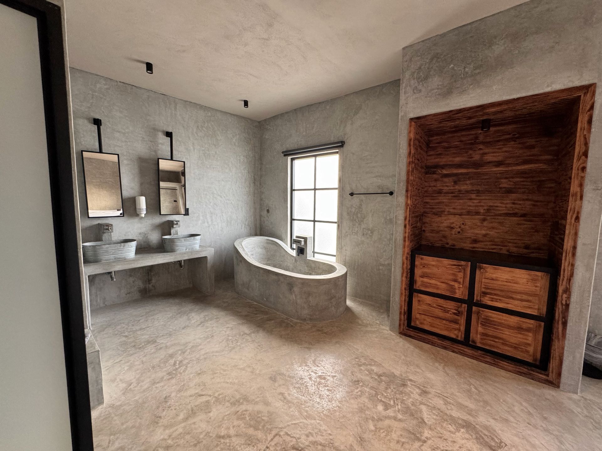 Baño rústico moderno con lavabo doble, bañera independiente, ventana y mueble de madera.