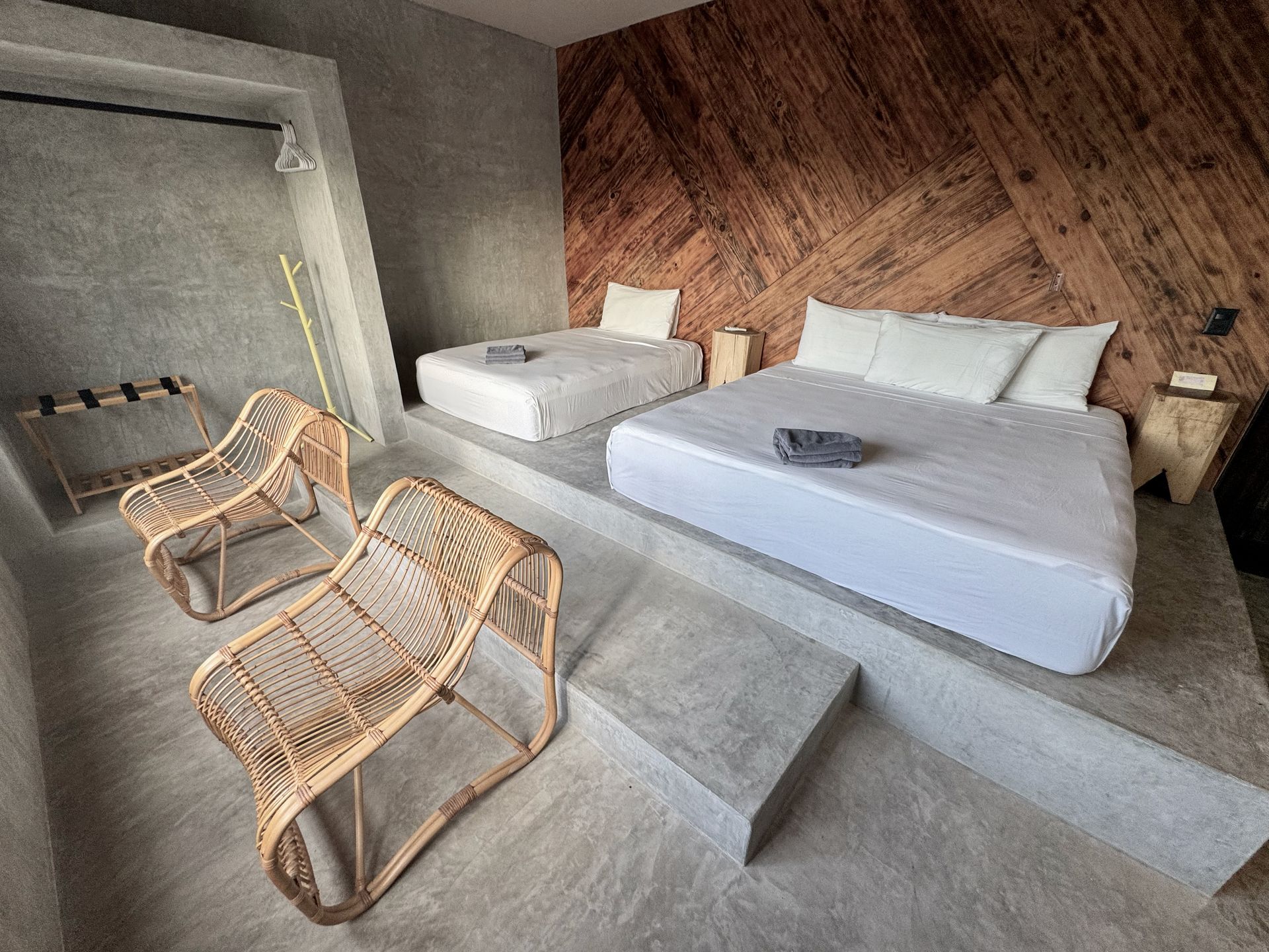 Dormitorio minimalista con dos camas, sillas de mimbre y escalones de hormigón.