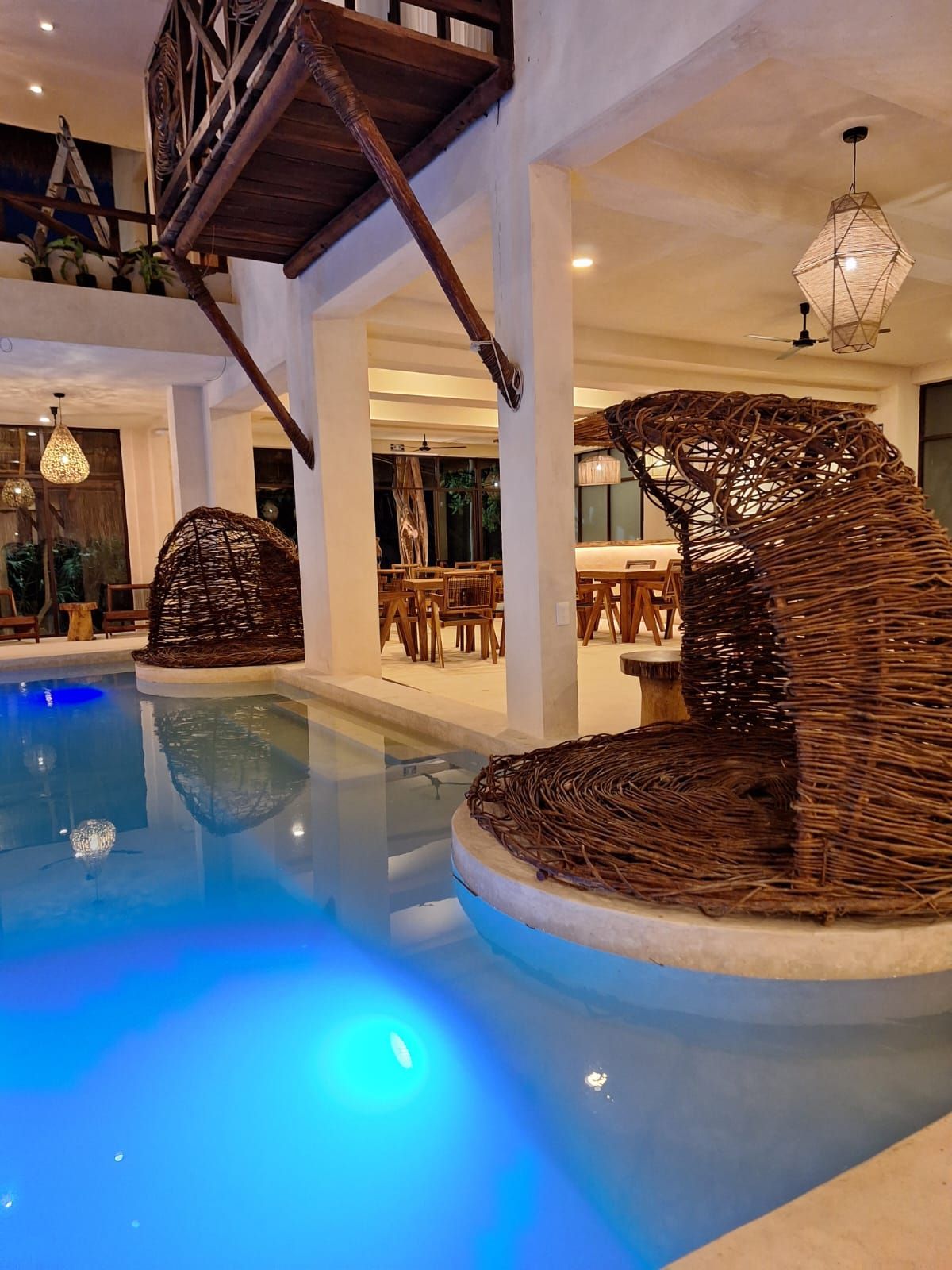 Piscina cubierta con agua azul brillante, tumbonas de mimbre y una cálida decoración de estilo resort tropical.