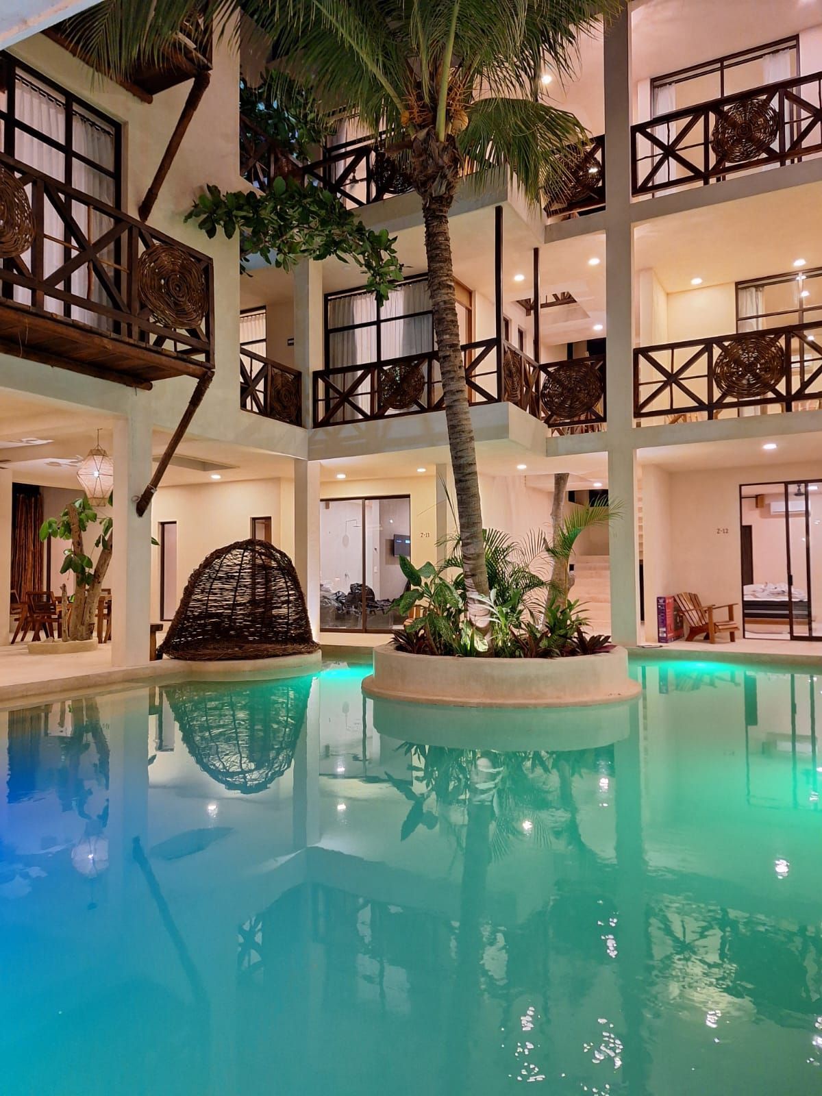 Patio interior del hotel con piscina turquesa, pasarelas en los balcones y exuberantes plantas tropicales.