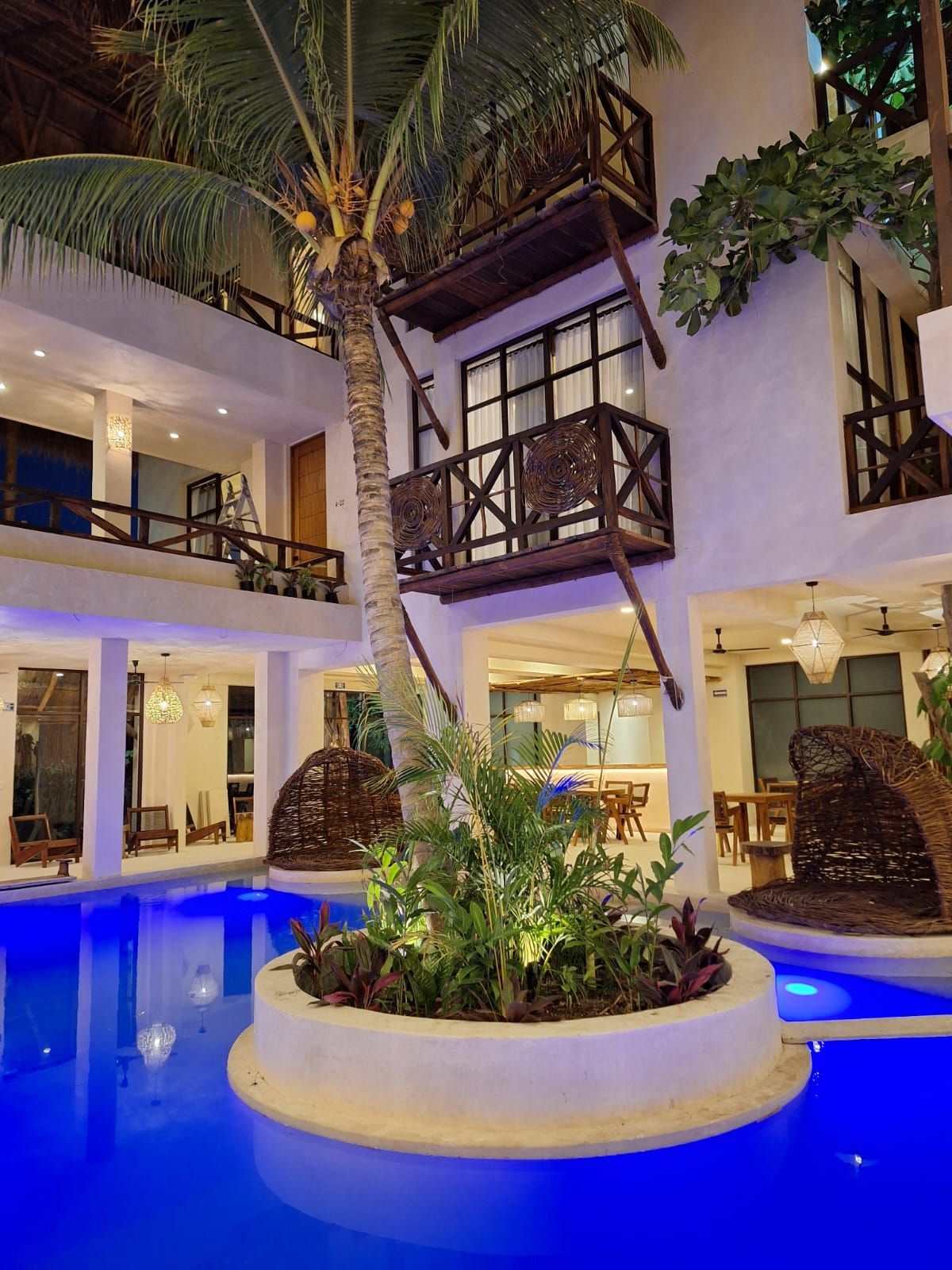 Patio de lujo con palmeras, piscina iluminada con luz azul y balcones por la noche.