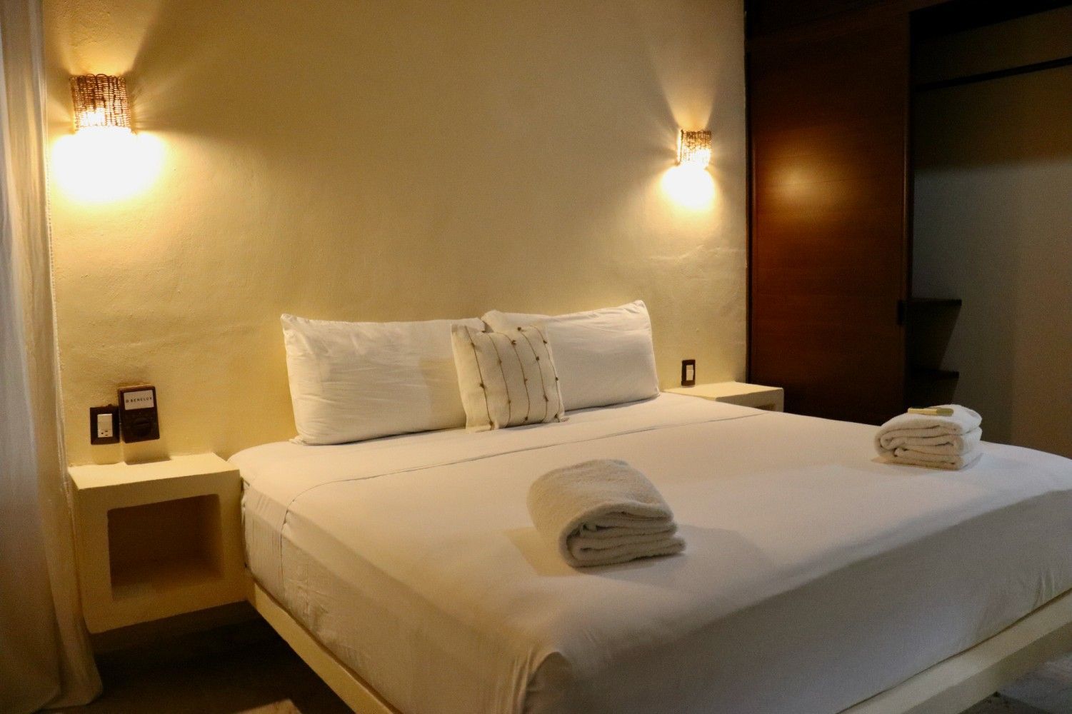 Habitación acogedora con una cama grande, apliques de pared y toallas dobladas sobre la cama.
