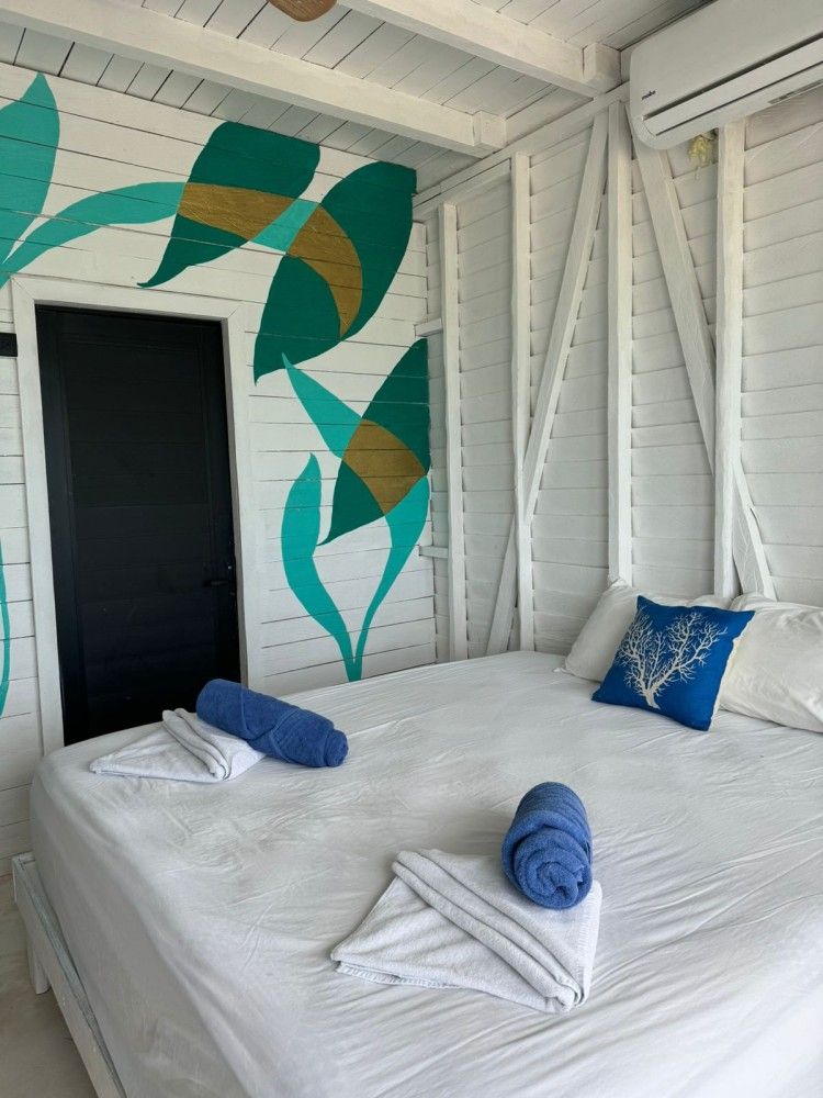 Habitación blanca con dos camas individuales, mural de pared color turquesa y toallas azules.