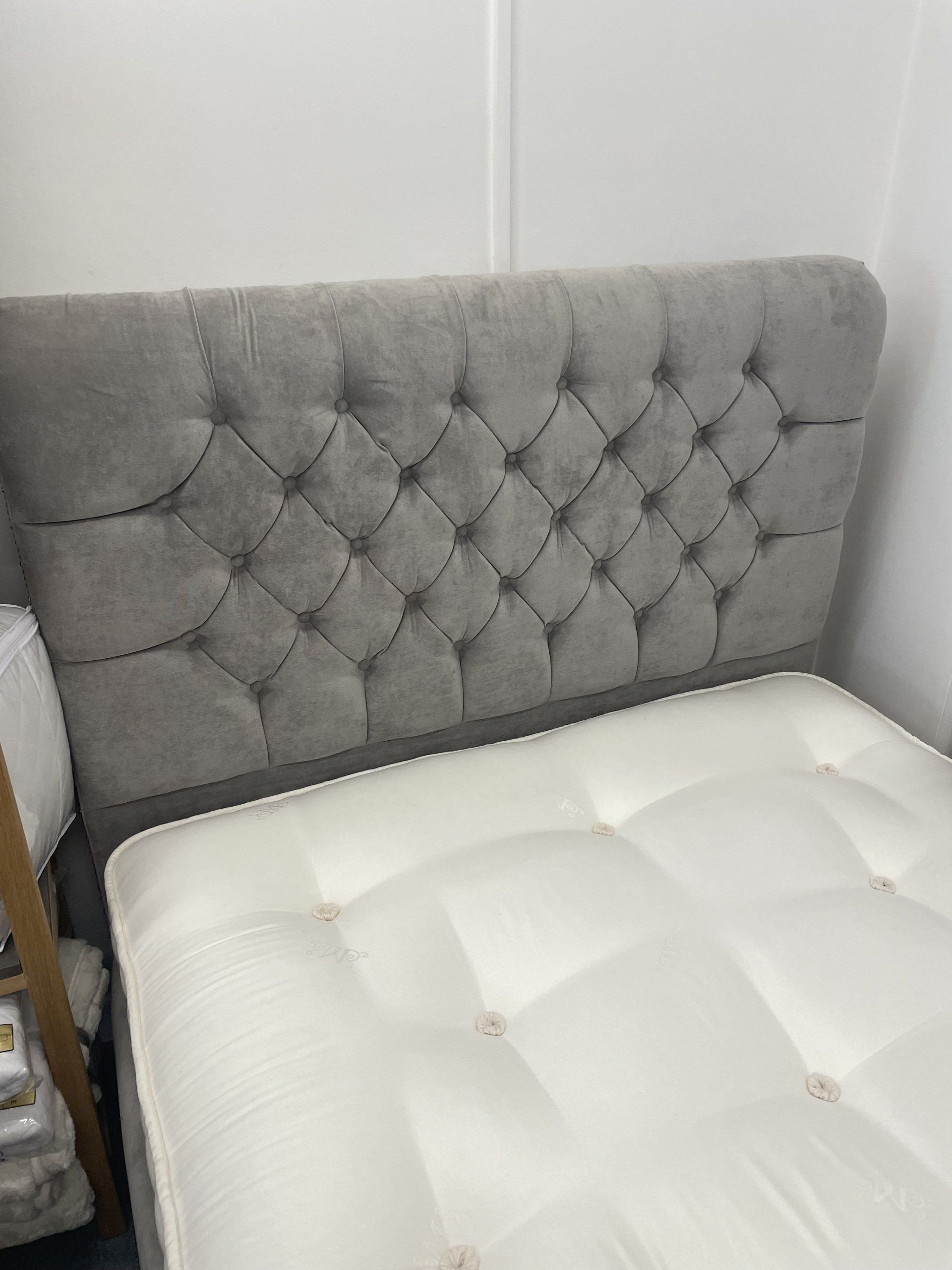 A bed with a grey headboard and a white mattress in a room.