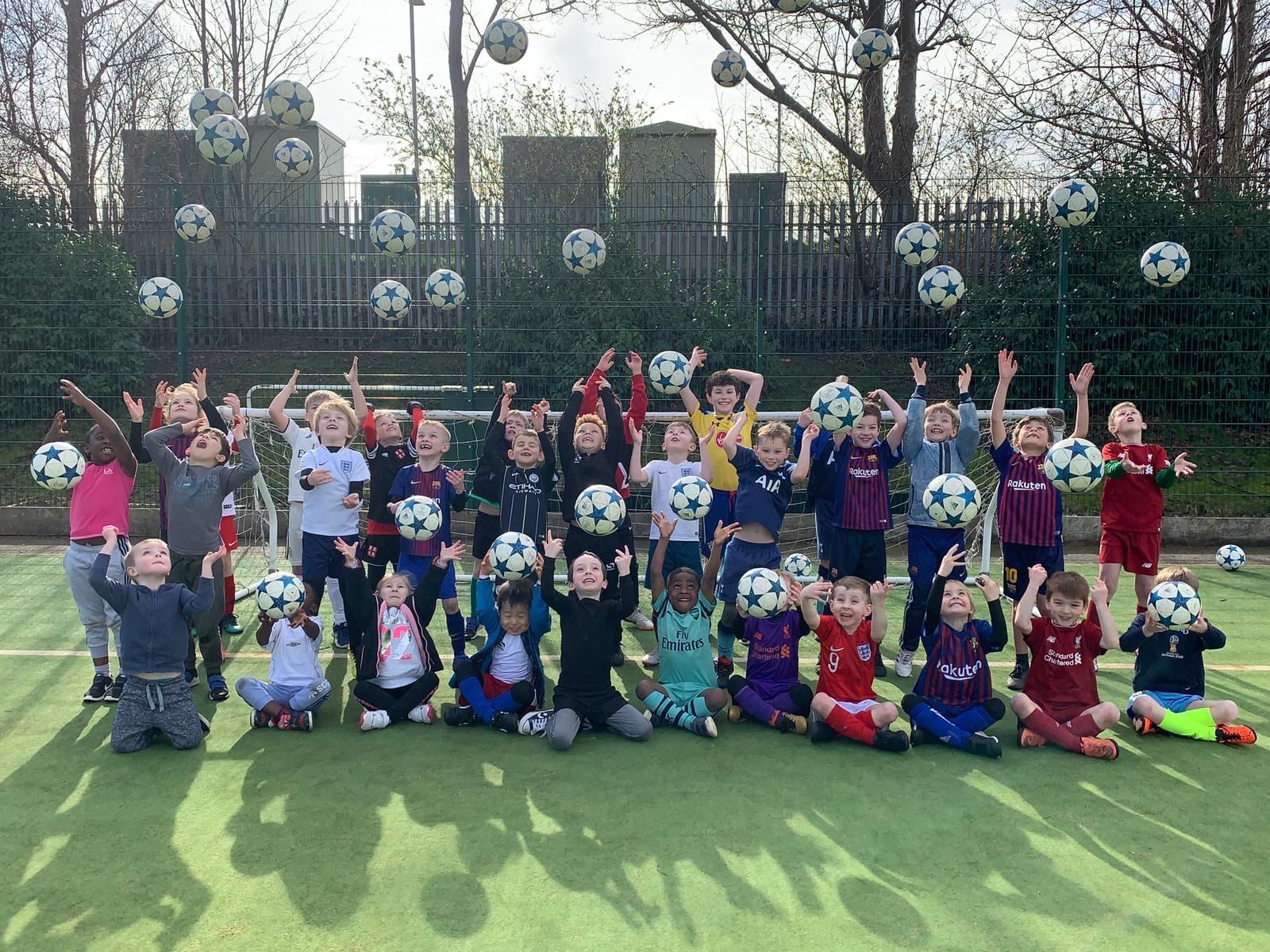 Children posing on a football field throwing footballs in the air, smiling with arms raised.