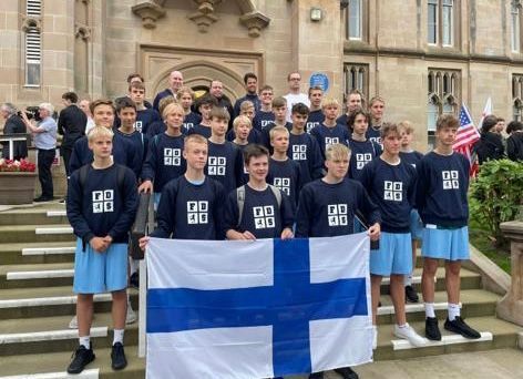 Group of people in navy sweatshirts holding a Finnish flag on stone steps outside a building