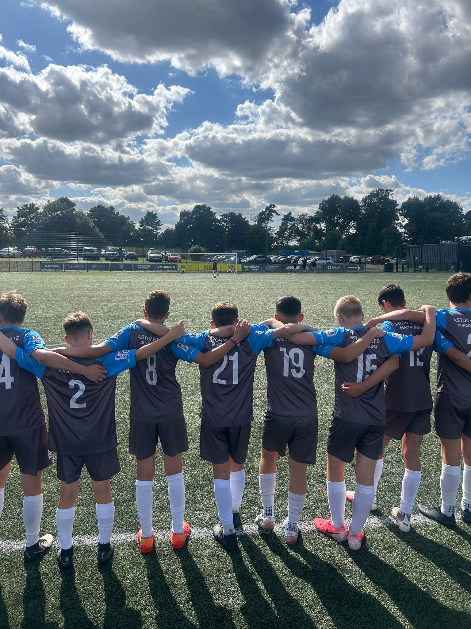 Football team in navy uniforms huddles on a field under a cloudy sky, facing the game ahead