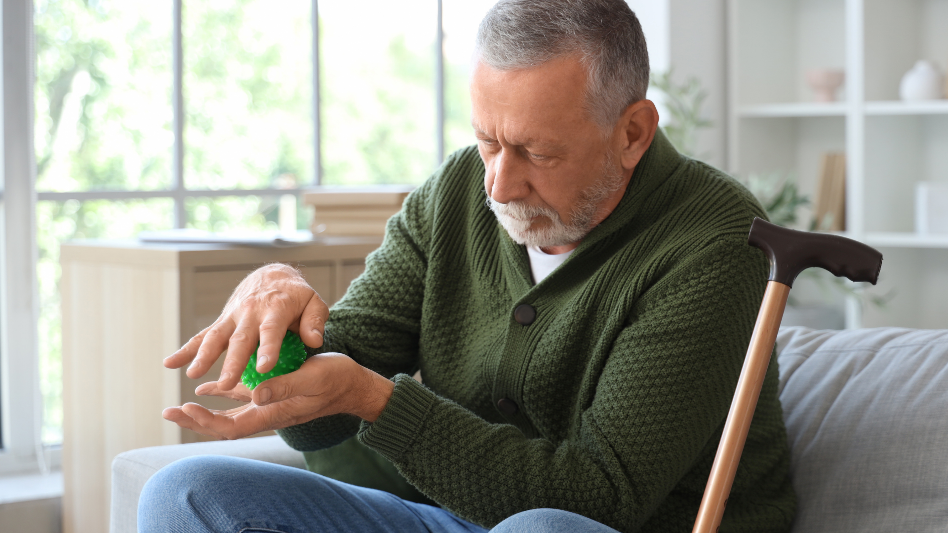 Older man sitting, examining medicine in his hand; cane nearby.