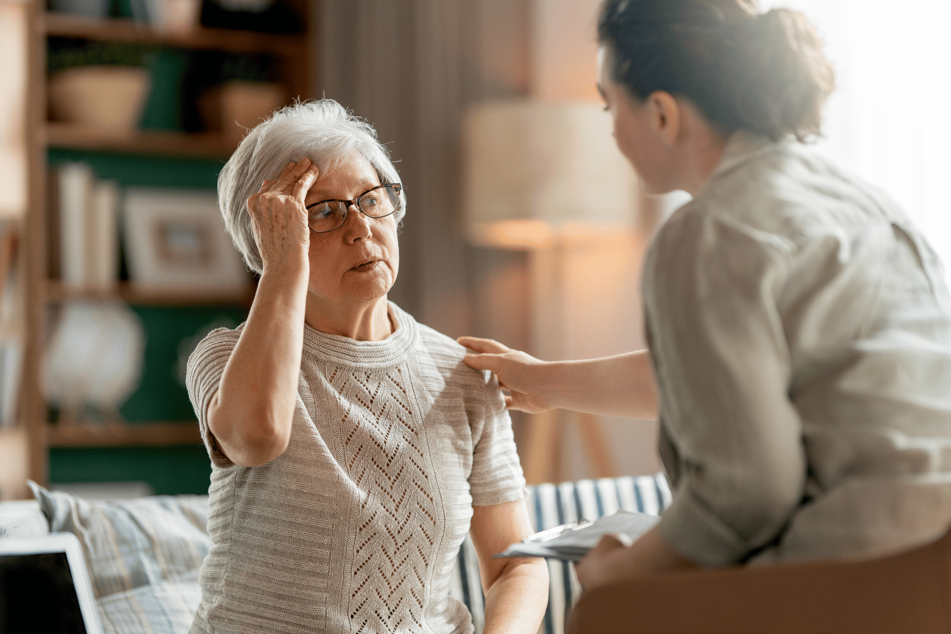 Elderly woman touching her head with a confused expression while a caregiver places her hand