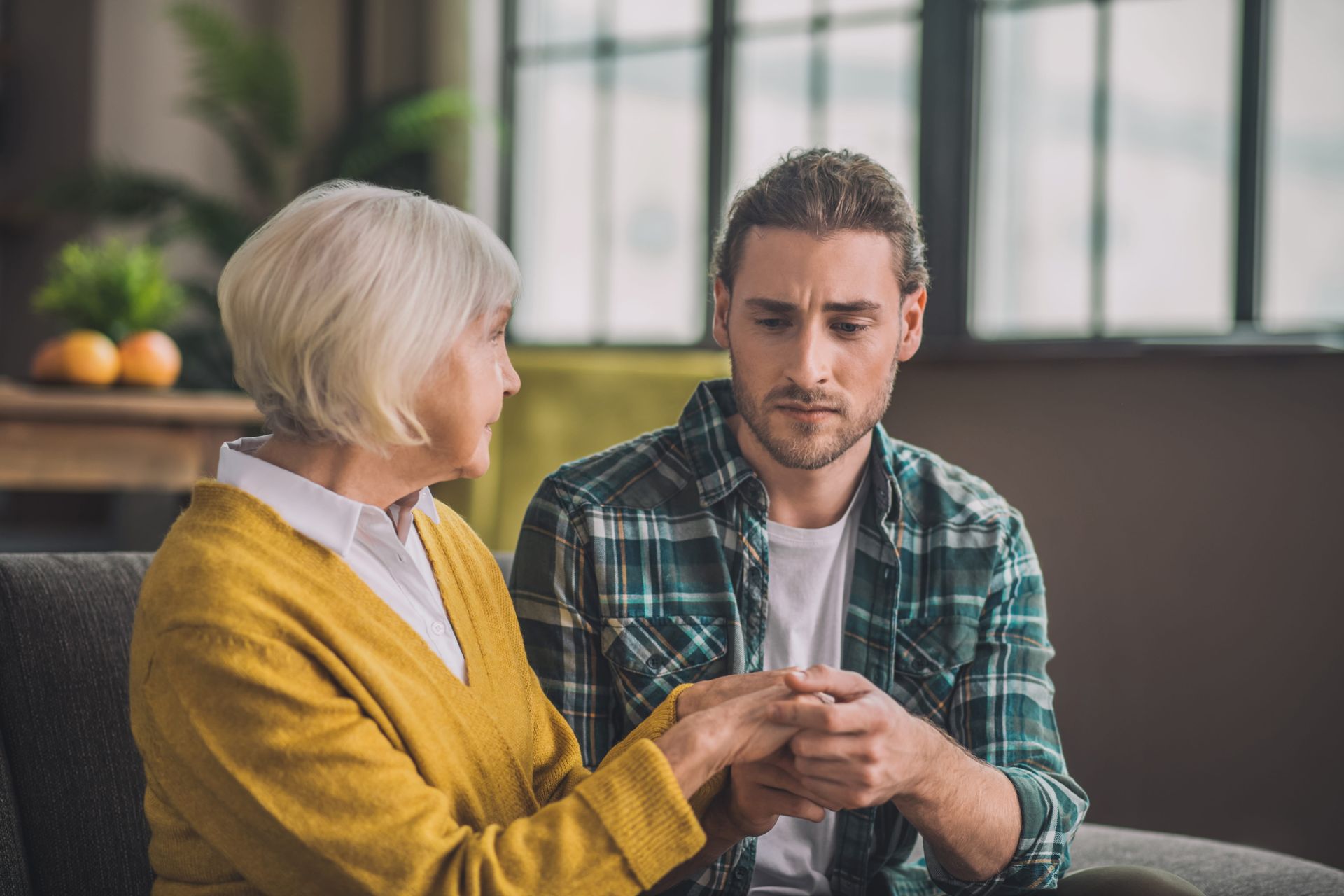 Adult son sitting quietly beside elderly mother with dementia