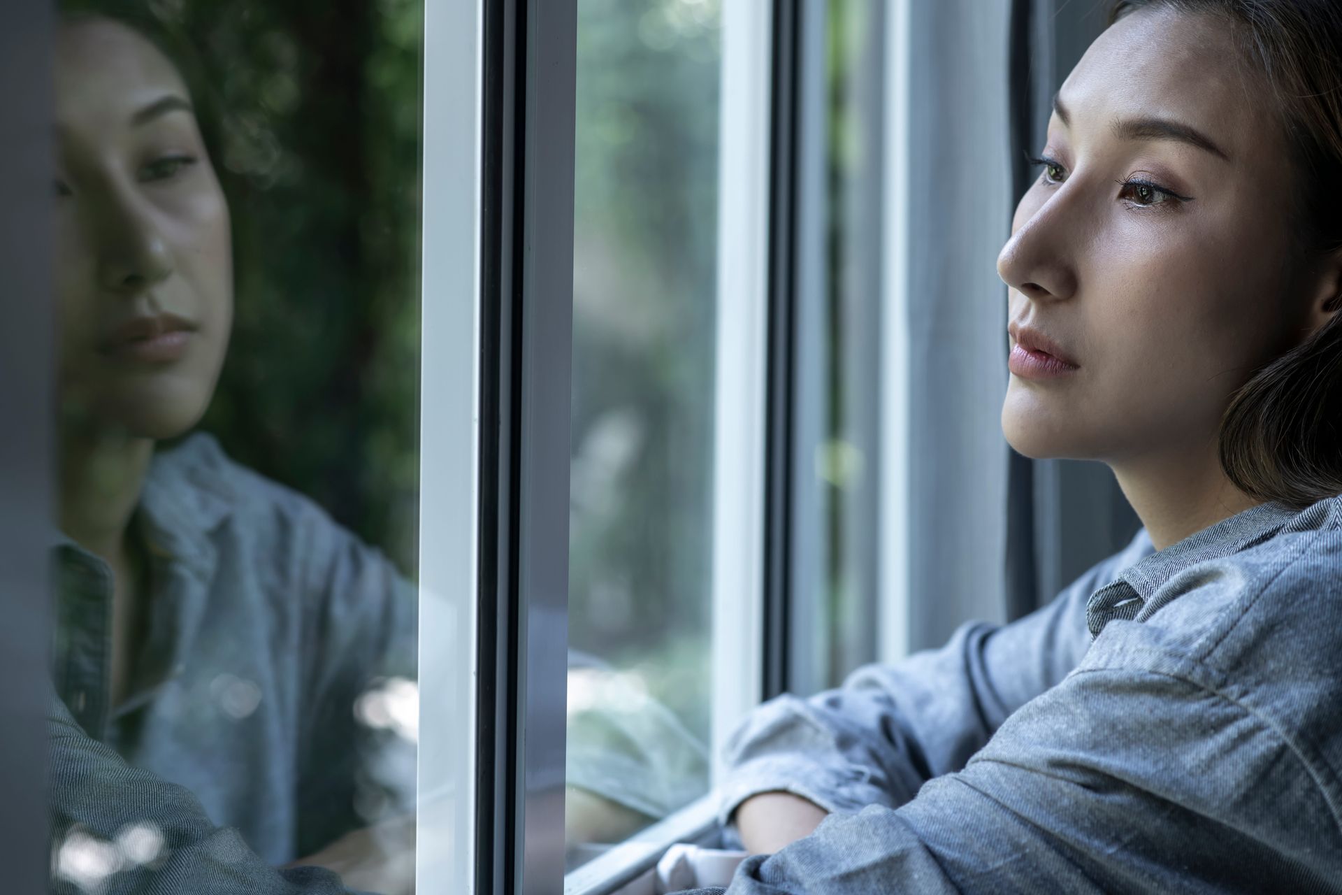 A woman sitting quietly by a window, looking reflective, representing the complicated grief