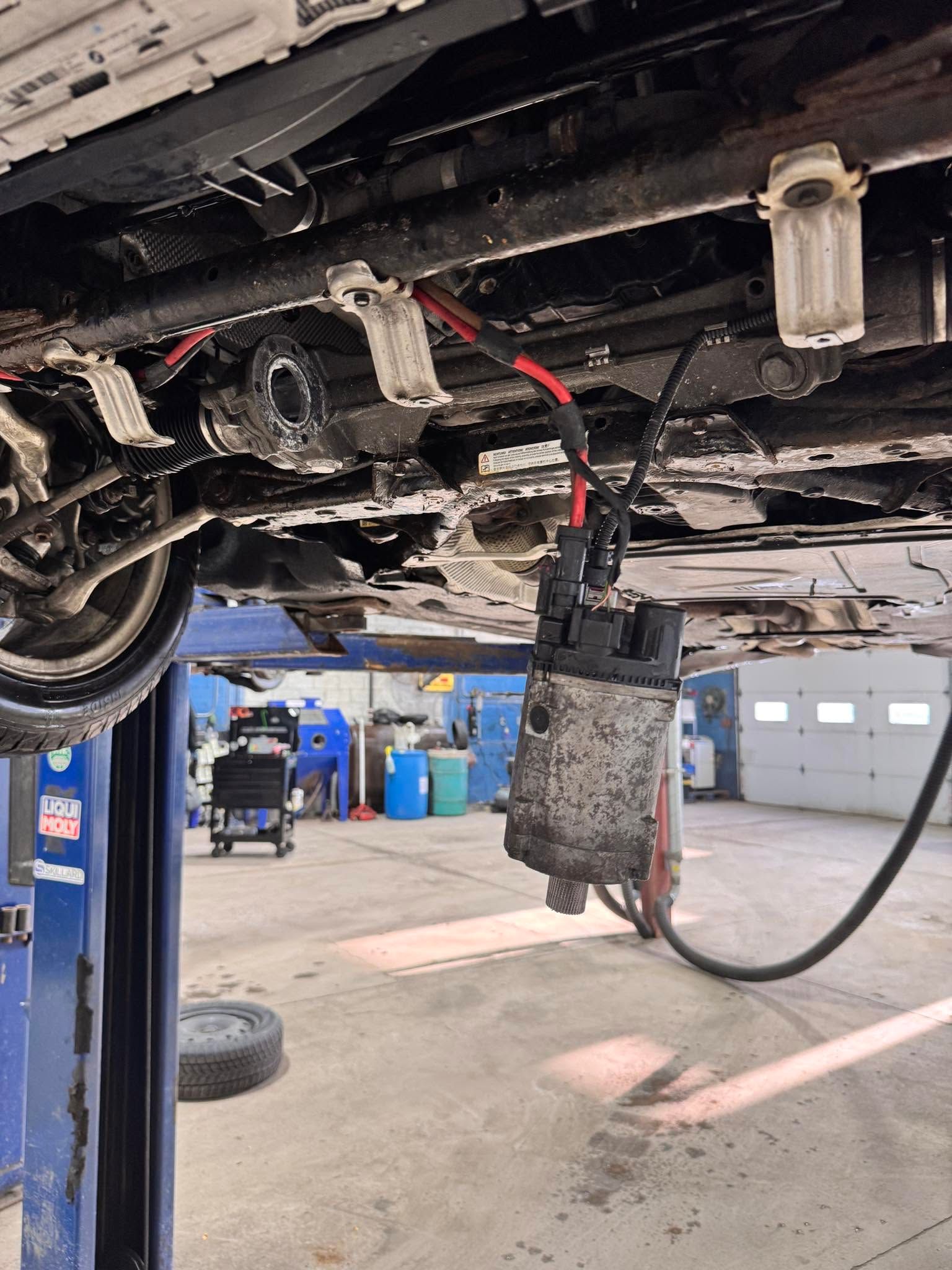 Undercarriage of a vehicle on a lift with a hanging metal component in an auto repair shop | SAI Automotive Inc.