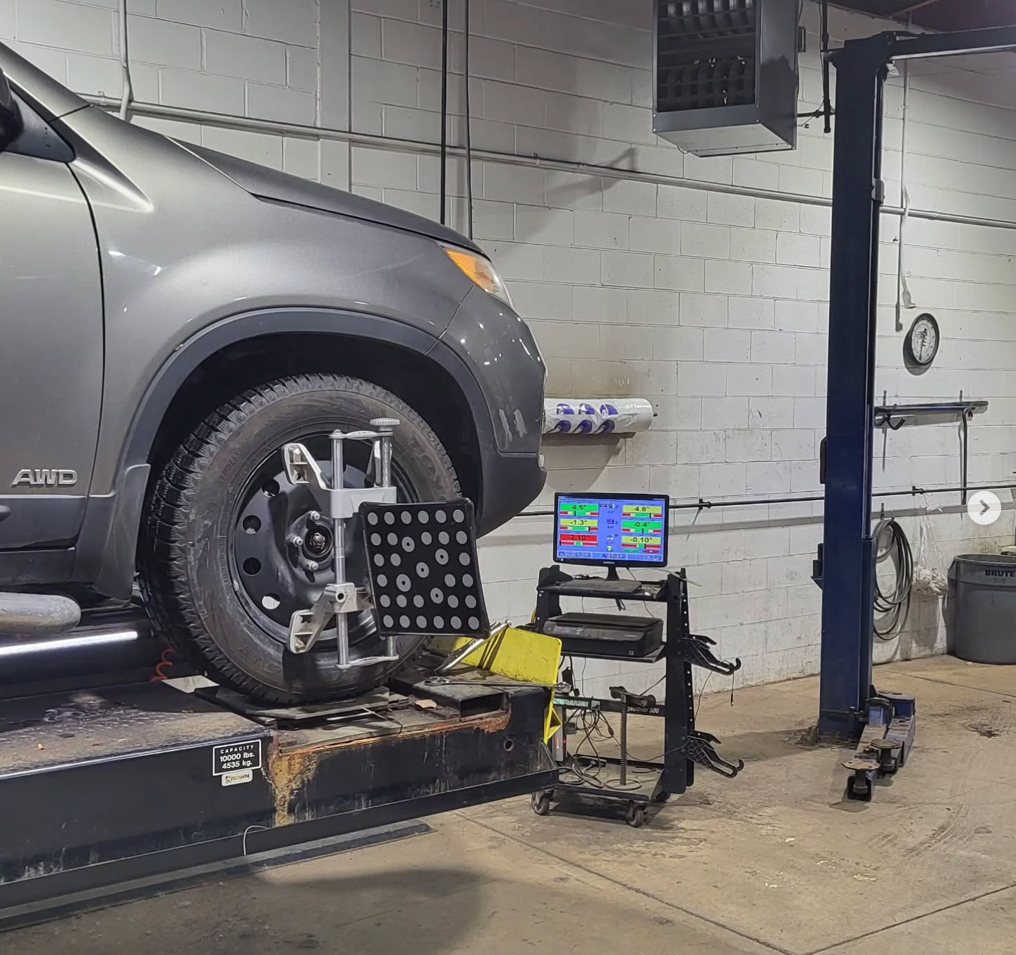 Gray SUV on a lift in an auto shop, with wheel alignment equipment and a laptop beside it | SAI Automotive Inc.