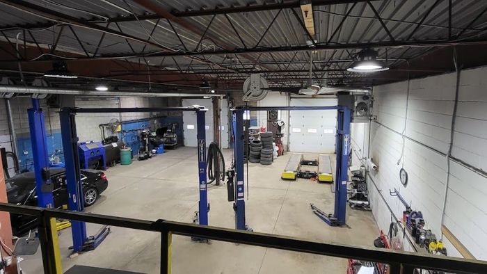 Large industrial garage with blue car lifts, tools, and equipment scattered around the open floor | SAI Automotive Inc.