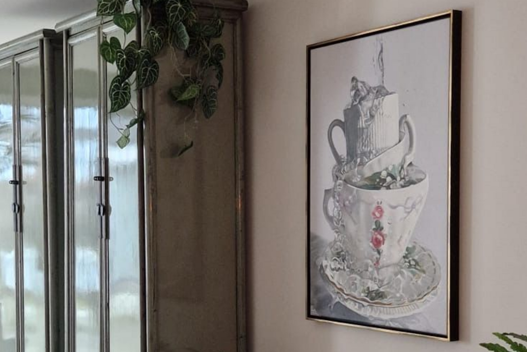 Ingelijste aquarel van een stapel theekopjes aan de muur, naast glazen kastdeuren en hangende planten.