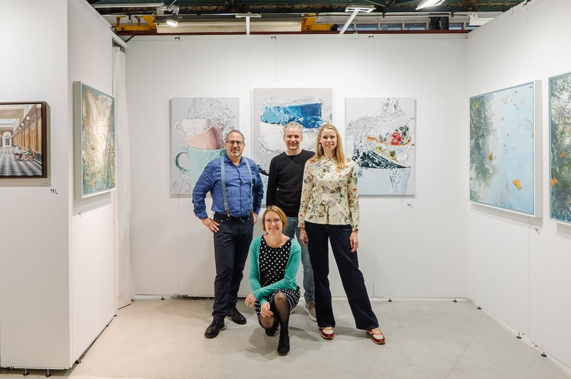 Vier mensen poseren in een kunstgalerie met abstracte schilderijen aan de muren