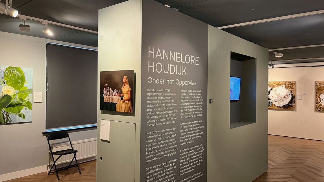 Interieur van het Huizer Museum met een grijze tentoonstellingswand, tekstpaneel, ingelijste kunstwerken en banken onder railverlichtiing