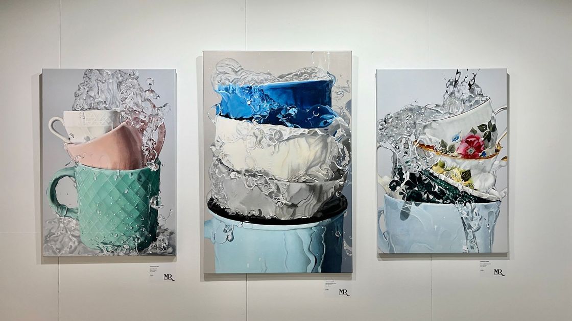 Drie abstracte schilderijen van koffiekopjes in pastel- en blauwtinten hangen aan een galeriemuur.