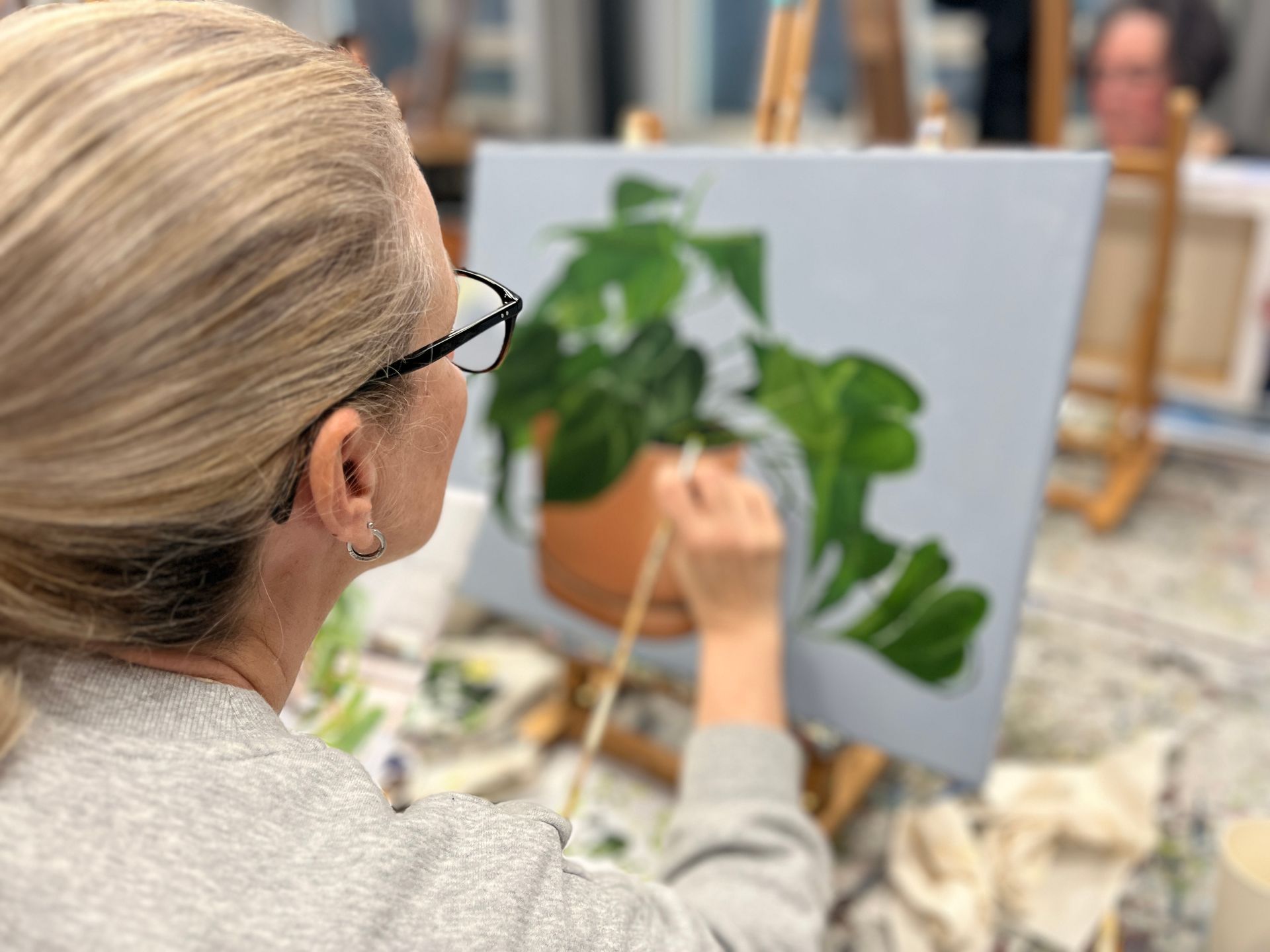 Iemand schildert een groene, bladerrijke plant op een doek in een kunststudio.