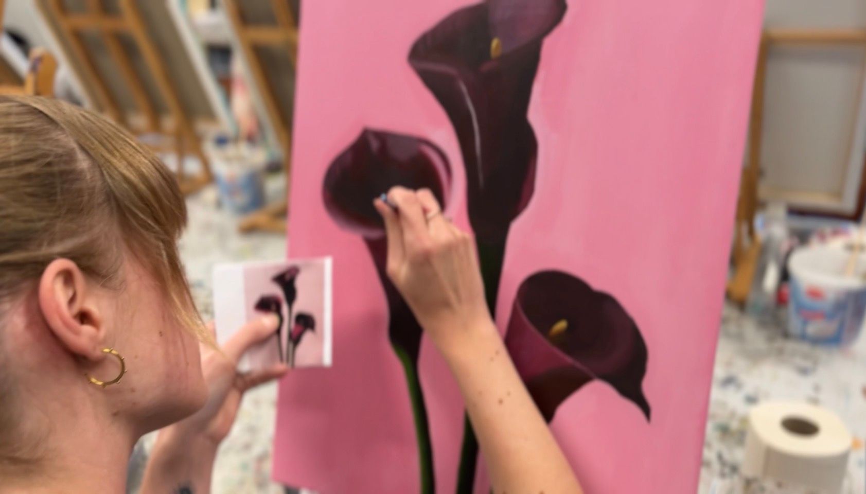 Kunstenaar schildert in een atelier op een roze canvas met donkere bloemvormen.