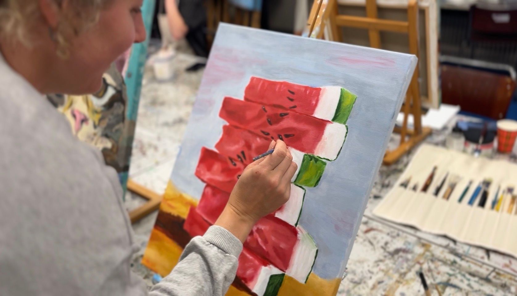 Kunstenaar schildert rode bloemen op een doek in een atelier, met penselen en verf binnen handbereik.