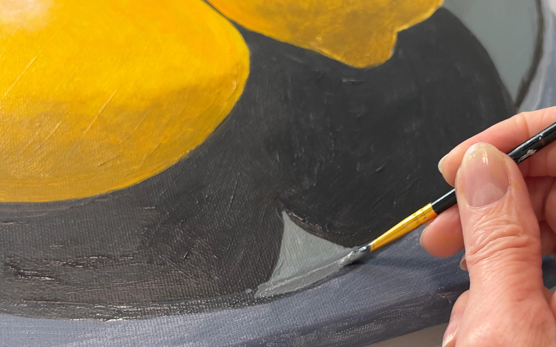 Een kwast met gele acrylverf  op een grijze schaal voor een online schildercursus.