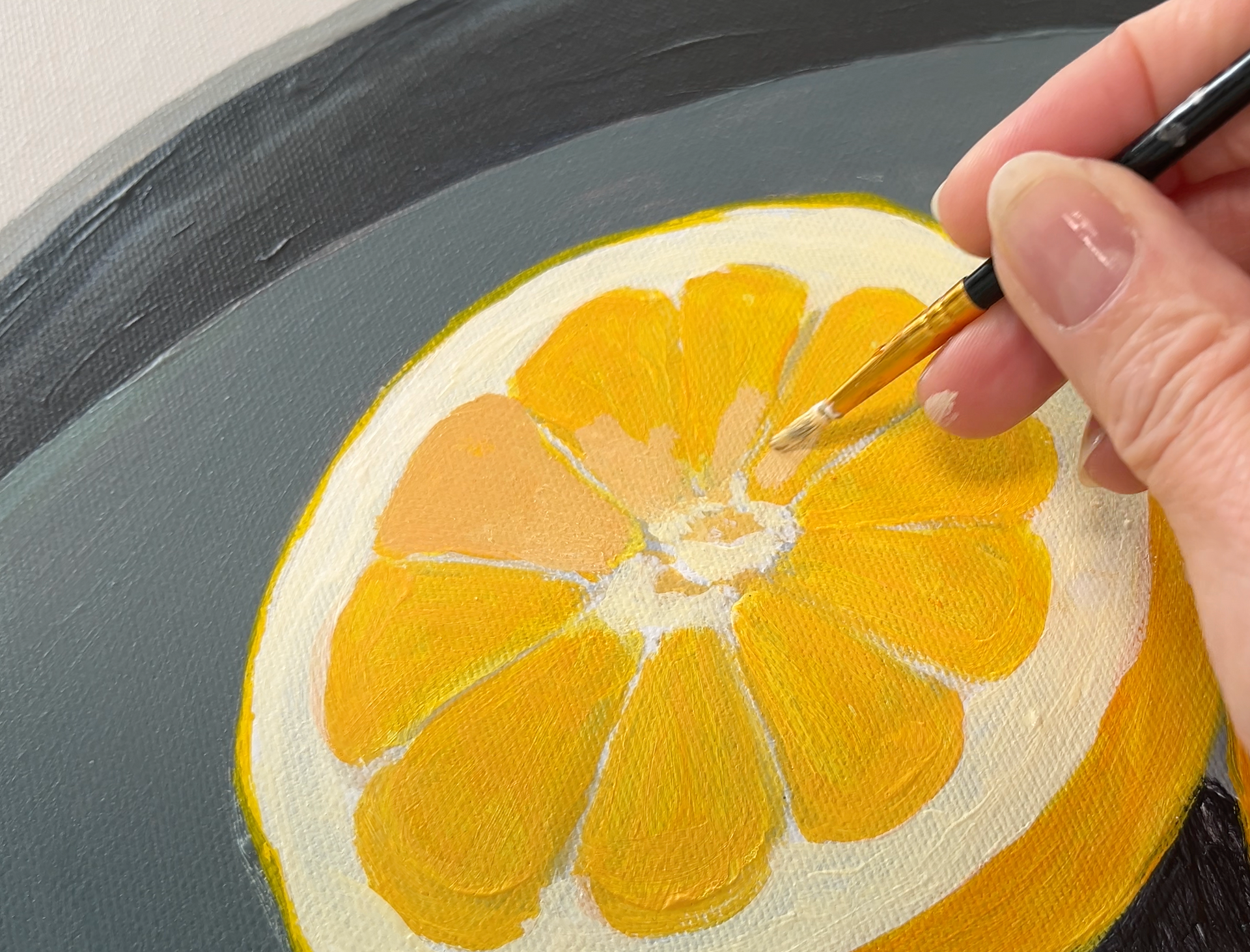 Een kwast met gele acrylverf  op een grijze schaal met citroenen voor een online schildercursus.