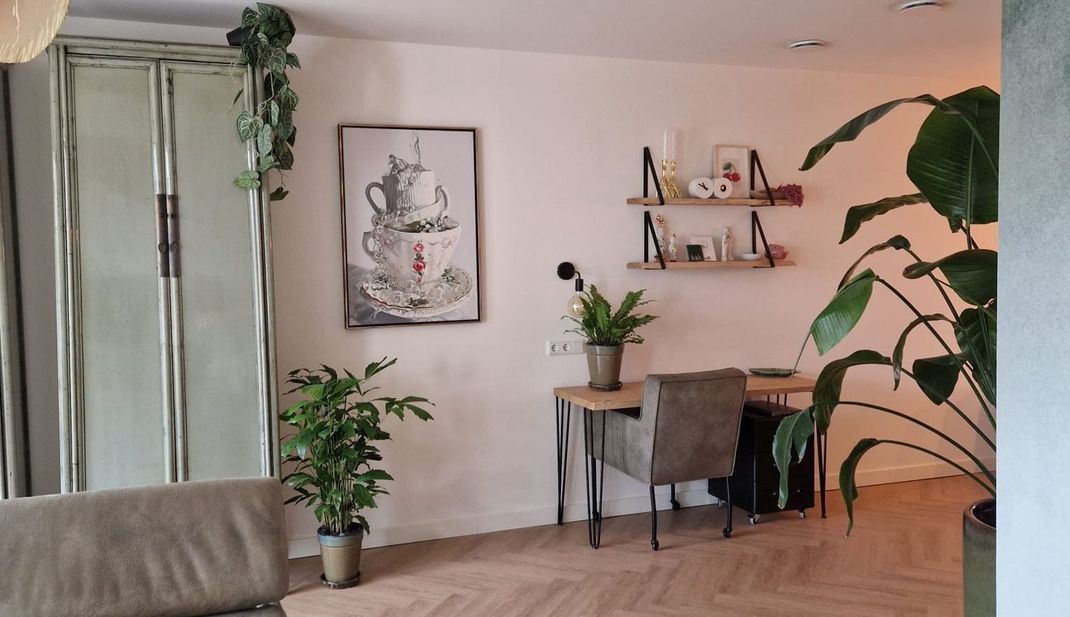 Gezellige thuiswerkplek met schilderij bureau, stoel, wanddecoratie, planten en zacht natuurlijk licht.