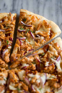 A pizza with chicken , onions and cheese is being cut into slices.