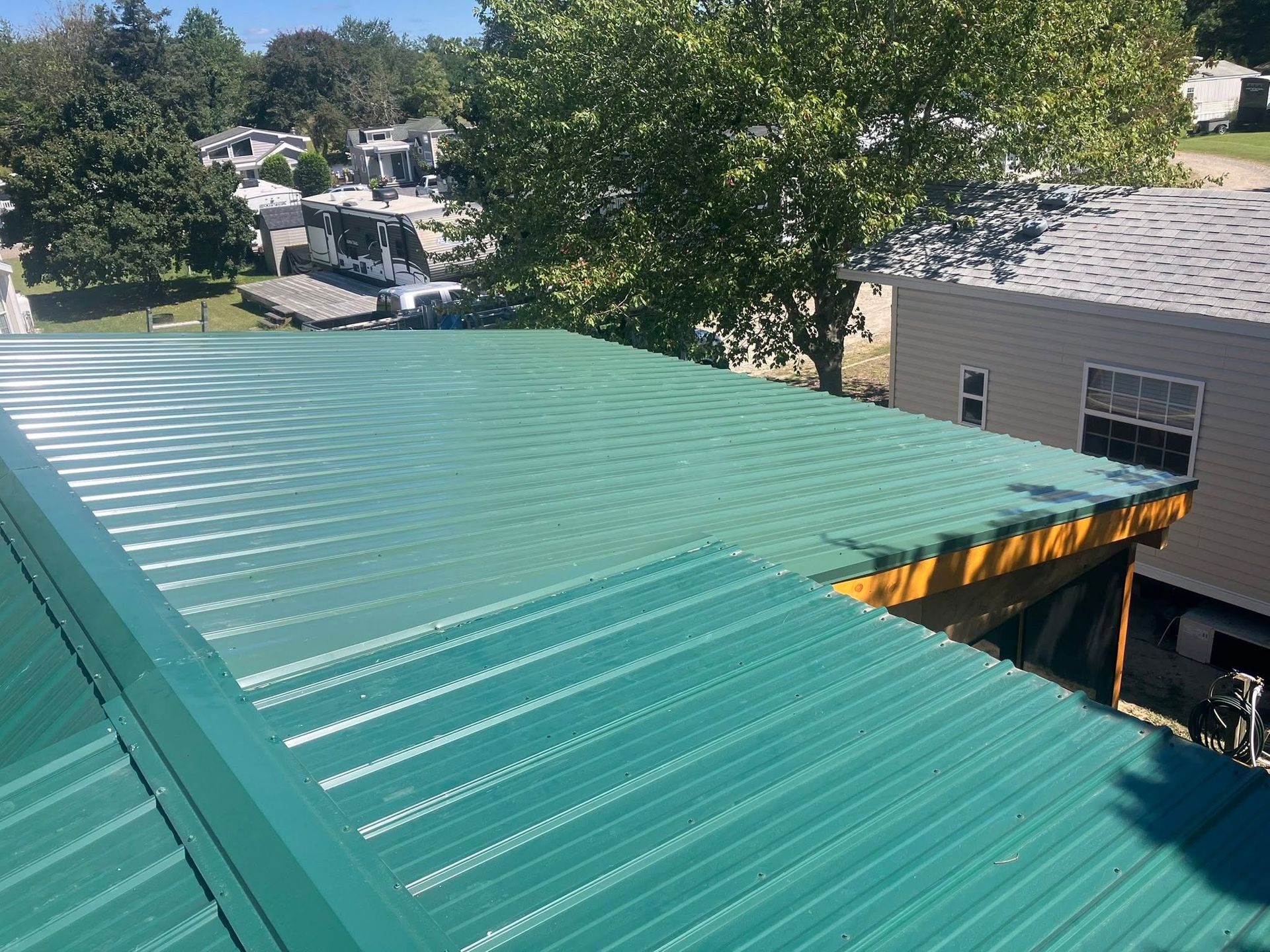 Green metal roof on a house beside trees and neighboring homes on a sunny day