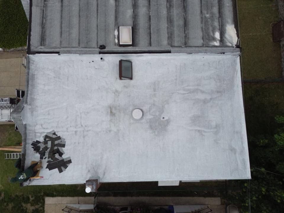 Aerial view of a large white roof with vents and a small tree shadow on the left side.