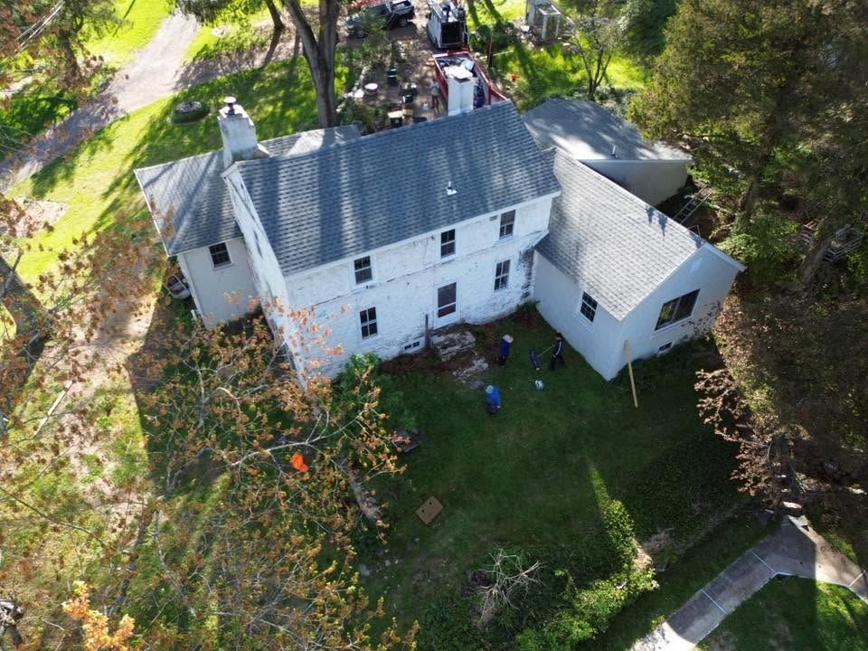 Aerial view of a white house with a gray roof, surrounded by trees and a grassy yard.