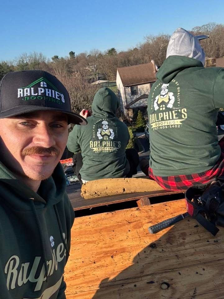 Three people in green Ralphie hoodies on a wooden structure outdoors on a sunny day