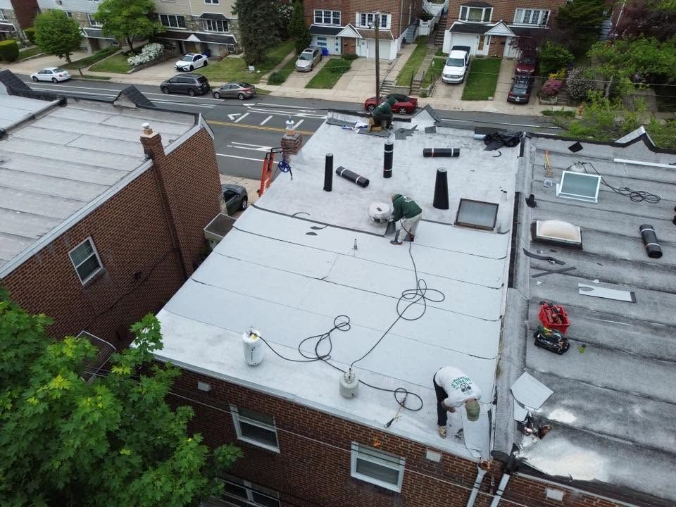 Aerial view of flat-roofed brick buildings with HVAC units, cables, and a residential street beyond.