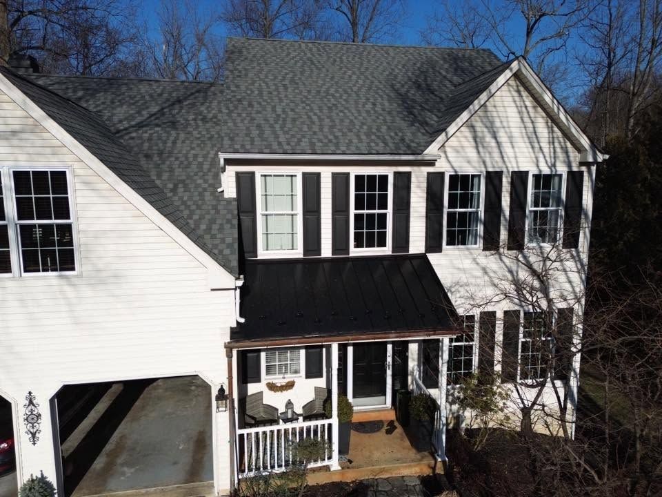 Two-story white house with black shutters, a black roof, and a covered front porch in daylight