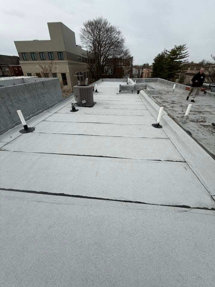 Snow-covered rooftop with vents and a building in the background under cloudy skies