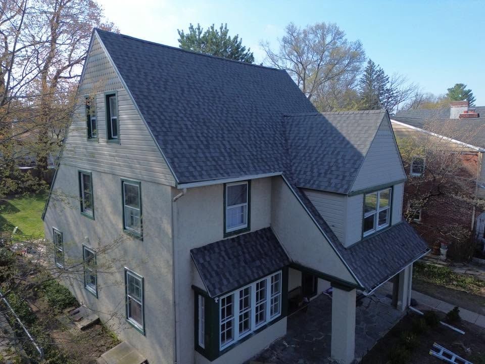 Two-story beige house with dark roof and covered porch, viewed from an elevated angle