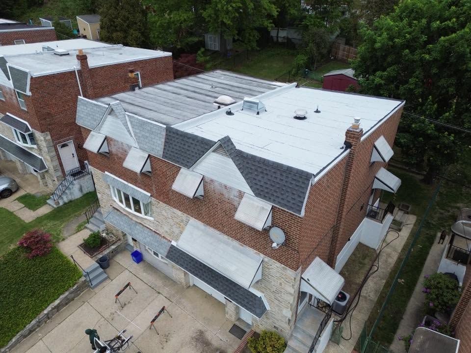 Aerial view of a brick house with a white roof and backyard patio, surrounded by trees.
