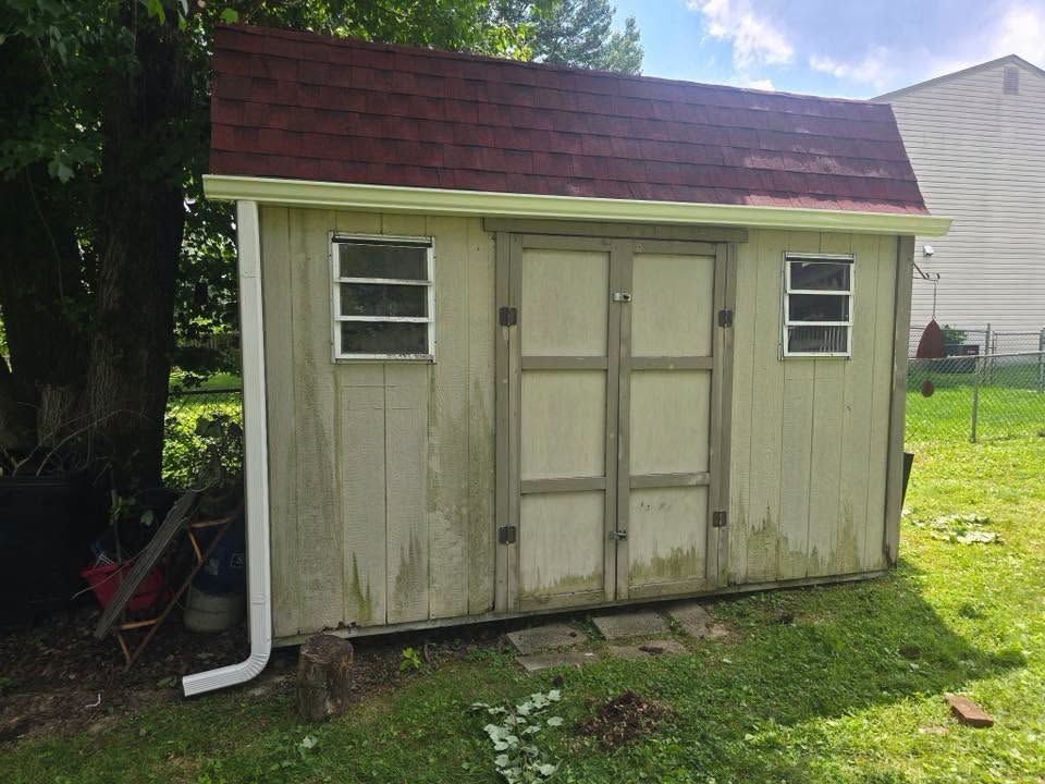 Small beige backyard shed with a red roof, white trim, and double doors on a grassy lawn.